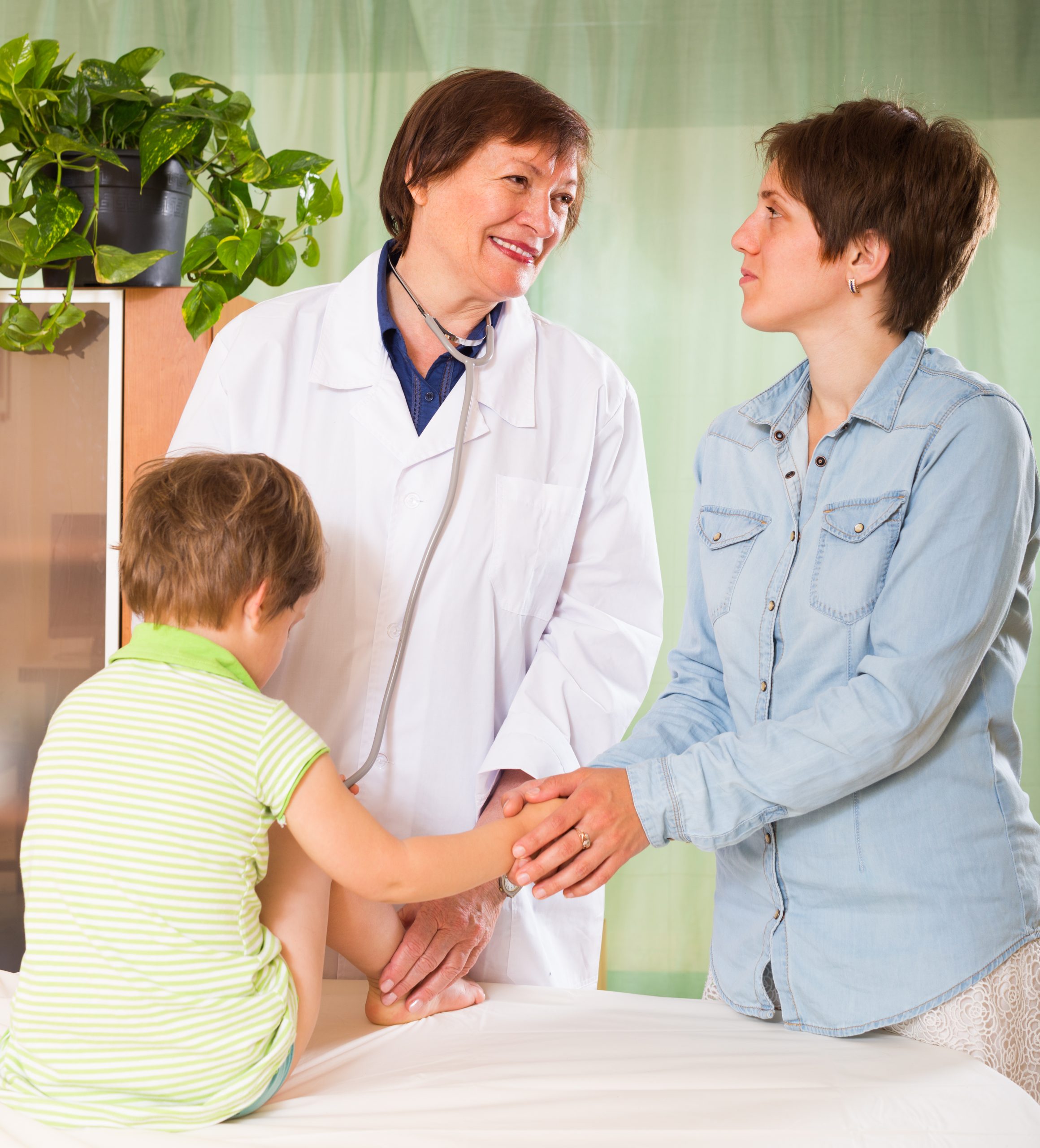 Smiling old female pediatrician doctor examining child at clinic
