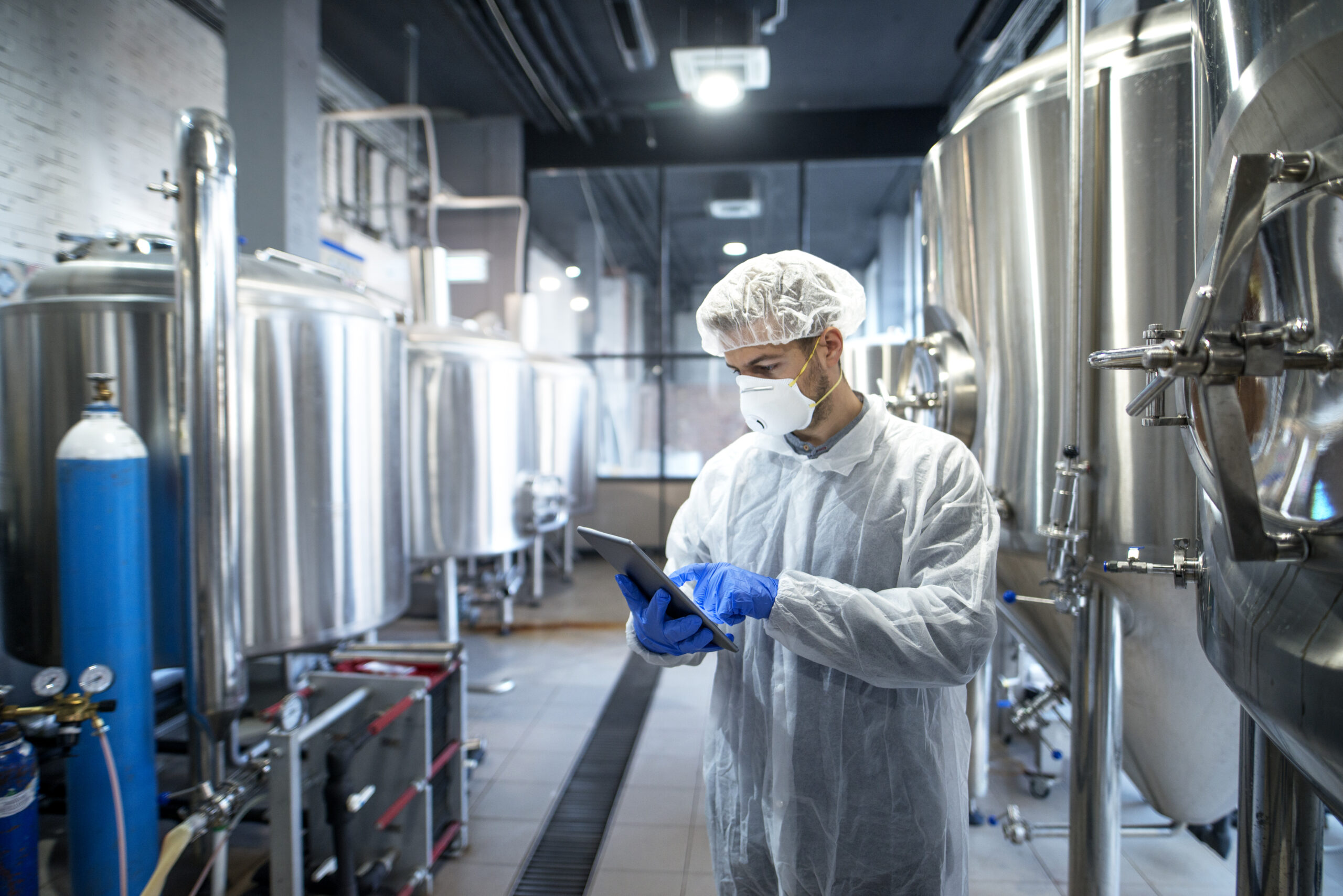 Technologist in white protective uniform controlling industrial process using tablet computer.